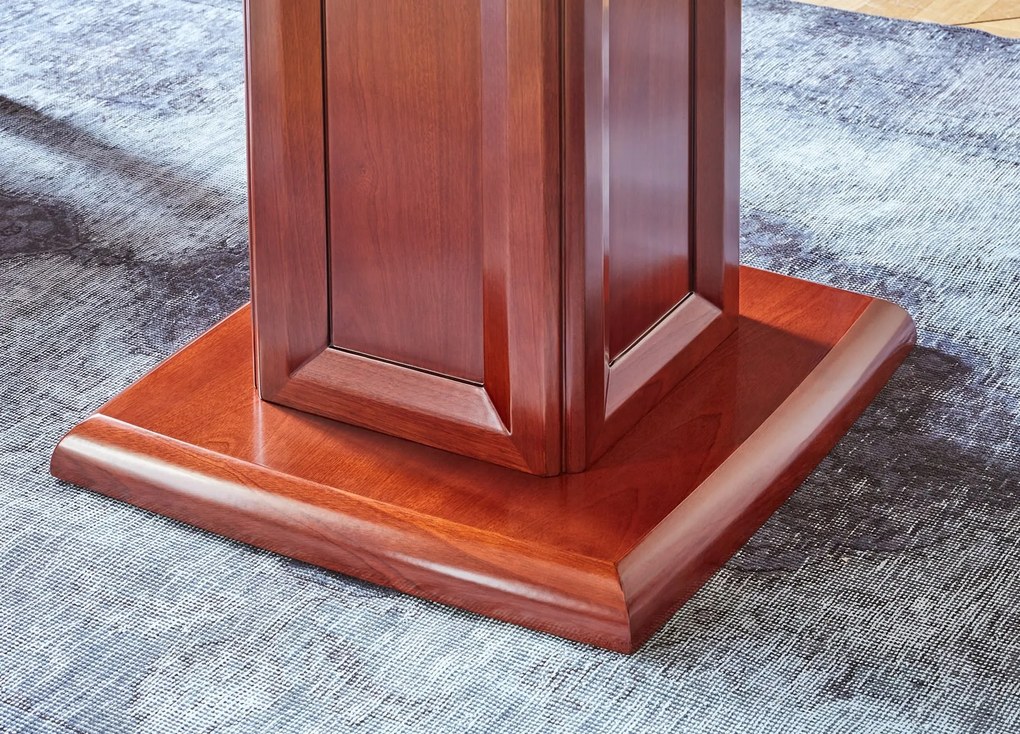 Elegancki stolik biurowy Visitor fornirowany drewnem w odcieniu koniaku. Stolik ma wymiary 100x100x75 cm. Kwadratowy blat na kolumnie zdobionej płycinami, rant frezowany. Klasyczny stolik do gabinetu.