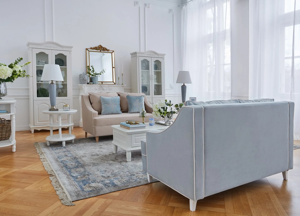 Kanapa sofa dwuosobowa do salonu. Sofa na drewnianych nóżkach, tapicerowana tkaniną welwetową. Sofa ma eleganckie podłokietniki, krawędzie obszyte kedrą, niebieska lub beżowa.