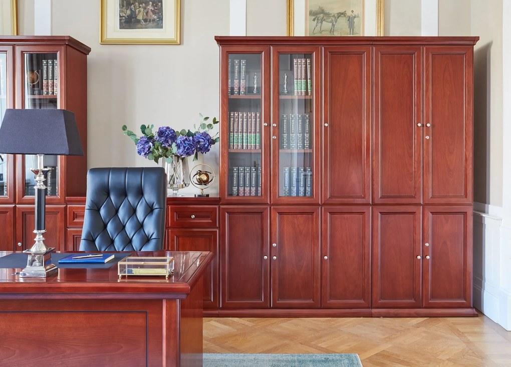 Elegancka szafa do biura Diamante. Szafa ma pełne drzwi, zamki na kluczyk, fronty wykończone płyciną, półki o regulowanej wysokości. Jest elegancko fornirowana na kolor koniaku, ma piękny cokół i gzyms.