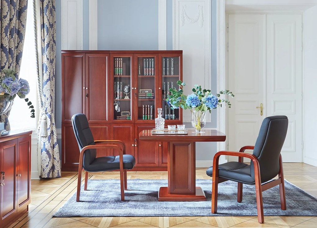 Elegancki stolik biurowy Visitor fornirowany drewnem w odcieniu koniaku. Stolik ma wymiary 100x100x75 cm. Kwadratowy blat na kolumnie zdobionej płycinami, rant frezowany. Klasyczny stolik do gabinetu.