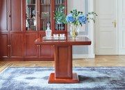 Elegancki stolik biurowy Visitor fornirowany drewnem w odcieniu koniaku. Stolik ma wymiary 100x100x75 cm. Kwadratowy blat na kolumnie zdobionej płycinami, rant frezowany. Klasyczny stolik do gabinetu.