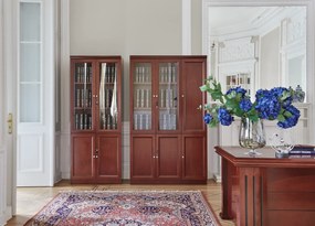 Klasyczna szafa do biura Elegance. Szafa ma górne drzwi częściowo przeszklone, dolne pełne, zamykane na kluczyk. Wymiary szafy 120x40x200 cm, kolor koniak, wykończona fornirem.